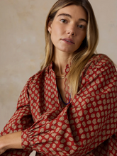 Load image into Gallery viewer, Close up shot of a woman wearing a red blouse with a tan geometric pattern against a beige wall