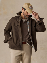 Load image into Gallery viewer, Man in a brown jacket lined with a striped pattern, styled with khaki pants and a baseball cap, standing in front of a beige background