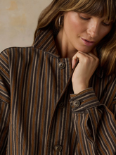 Load image into Gallery viewer, A close-up of a woman wearing a brown and beige vertically striped button-up shirt with a high collar and textured fabric.
