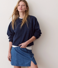 Load image into Gallery viewer, A woman wearing a dark navy blue crewneck sweatshirt and a blue denim mini skirt with a side slit, posing against a plain off-white wall.