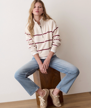 Load image into Gallery viewer, A woman sits on a wooden block wearing a cream quarter-zip pullover with burgundy stripes, light-wash blue jeans, and beige sneakers against a plain off-white wall.