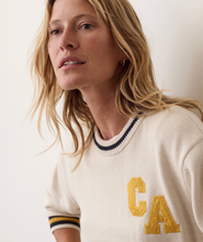 Load image into Gallery viewer, A close-up of a woman wearing a cream-colored knit sweater with yellow embroidered letters 'CA' on the chest and navy and yellow striped ribbed trim at the collar and cuffs.