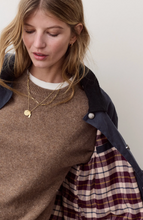 Load image into Gallery viewer, A close-up lifestyle shot of a woman wearing a brown knit crewneck sweater, layered with a navy blue jacket that has a red and beige plaid lining. She is accessorized with gold necklaces.