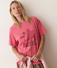 Load image into Gallery viewer, A woman wearing a pink -red graphic t-shirt with a bridge design and the words 'Stay Golden' in gold script, posed against a plain beige wall.