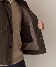 Load image into Gallery viewer, A close-up of a person wearing an olive green jacket over a beige knit sweater, with the jacket open to show the interior lining and pocket. A hand is visible holding the jacket open against a plain beige background.