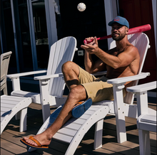 Load image into Gallery viewer, Man wearing leather flip flops sitting on a white chair holding a red baseball bat with a ball in the air