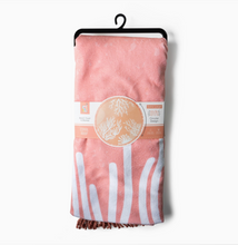 Load image into Gallery viewer, A pink plush beach towel blanket with white patten and a fringed edge, hanging from a black hanger against a light gray background. A paper label wraps around the middle of the blanket.