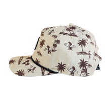 Load image into Gallery viewer, A beige baseball cap with a brown palm tree and surfer pattern, shown from a three-quarters angle on a white background.