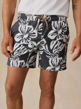 Load image into Gallery viewer, Man standing with a white tee and black &amp; white floral print shorts on a tan background
