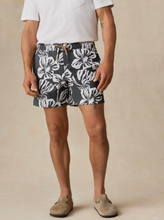 Load image into Gallery viewer, Man standing with a white tee and black &amp; white floral print shorts on a tan background
