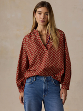 Load image into Gallery viewer, Woman standing wearing a red blouse with a tan geometric pattern, tucked into jeans, against a beige wall
