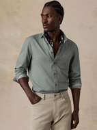 Man wearing a sage green button down shirt with khaki pants in front of a beige wall