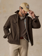 Man in a brown jacket lined with a striped pattern, styled with khaki pants and a baseball cap, standing in front of a beige background