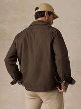 Load image into Gallery viewer, Back view of a man in a brown jacket styled with khaki pants and a baseball cap, standing in front of a beige background

