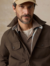 Load image into Gallery viewer, Closeup view of a man in a brown jacket lined with a striped pattern, styled with a polo and a baseball cap, standing in front of a beige background
