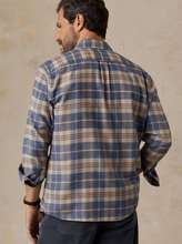 Load image into Gallery viewer, Back view of a man in a tan and blue plaid button down shirt and dark pants, standing in front of a beige wall 
