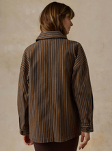 Load image into Gallery viewer, A woman shown from the back wearing a brown and beige vertically striped button-up shirt jacket, set against a textured beige wall.
