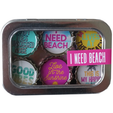 Load image into Gallery viewer, A square metal tin containing six circular bottle-cap-style magnets with beach-themed quotes, including 'I NEED BEACH,' 'LIVES AT THE BEACH,' 'GOOD VIBES,' and 'Live in the Sunshine.'.
