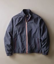 Load image into Gallery viewer, A dark slate blue zip-up jacket with a red, white, and blue striped zipper and matching striped pocket trim, laid flat against a neutral beige background.
