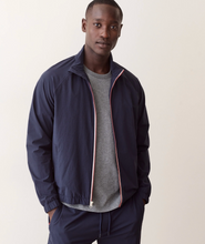Load image into Gallery viewer, A man wearing a navy blue zip-up jacket with pink and white piping trim, layered over a gray crewneck t-shirt and matching navy pants, standing against a plain light beige background.
