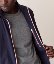 Load image into Gallery viewer, Close-up of a person wearing a navy lightweight zip jacket over a heather gray crewneck shirt, with the jacket being opened to show the lining and zipper detail.
