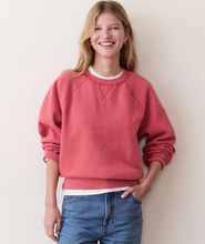 Load image into Gallery viewer, A smiling woman wearing a dusty rose crewneck sweatshirt over a white undershirt and blue jeans, standing against a plain light beige wall.

