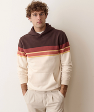 Load image into Gallery viewer, A man wearing a brown and cream striped hoodie with gold accent stripes, paired with cream trousers, standing against a plain off-white wall.
