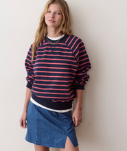 Load image into Gallery viewer, A woman wearing a navy and coral pink striped long-sleeve sweatshirt and a blue denim mini skirt, standing against a plain light beige wall.
