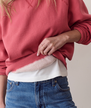 Load image into Gallery viewer, A close-up of a person wearing a dusty rose pink crewneck sweatshirt with a white t-shirt and blue jeans, showing the soft fleece lining of the sweatshirt being pulled up by the hand.
