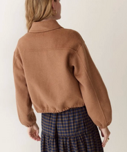 Load image into Gallery viewer, Back view of a woman wearing a camel colored wool zip front jacket over a plaid skirt in front of a plain cream background 
