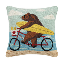 Load image into Gallery viewer, A square hook-and-loop rug pillow featuring a brown bear riding a red bicycle while carrying a yellow surfboard, set against a light blue sky with white clouds and a sandy beige ground.
