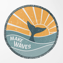 Load image into Gallery viewer, A round beach towel with a fringed edge featuring a retro-style graphic of a whale tail surfacing from the water under a yellow-orange sun, with the text 'MAKE WAVES' in white on a gray-blue wave, set against a light gray background.
