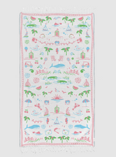 Load image into Gallery viewer, A rectangular white beach towel with fringed edges, featuring a colorful all-over seaside pattern with palm trees, sailboats, umbrellas, waves, and small buildings, shown flat against a light gray background.
