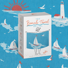 Load image into Gallery viewer, A boxed Turkish Beach Towel set from the brand Turquoise, featuring a white box with a clear window showing a blue towel with a beach-themed illustration, set against a matching blue patterned background.
